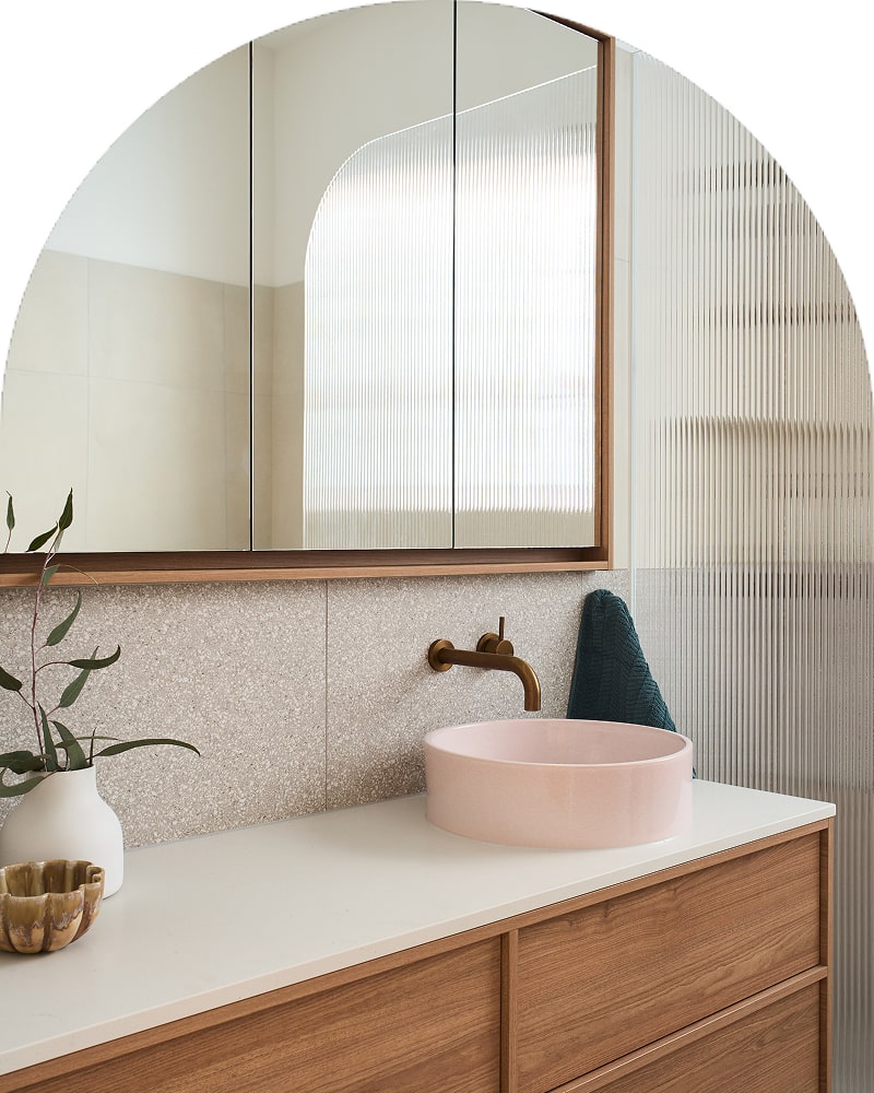 A sleek, stylish bathroom featuring a pink basin, wooden vanity, and dark brushed metal tapware.