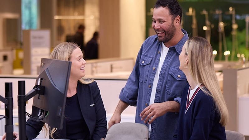 A couple happily speaking with a Reece Bathrooms showroom consultant at a desk with a monitor