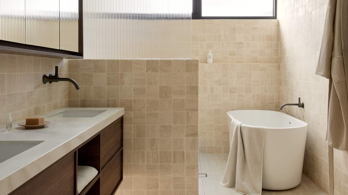 A spa-like bathroom featuring neutral tile, freestanding bath next to an expansive shower area, and timber vanity with double basins, mirror and gunmetal tapware