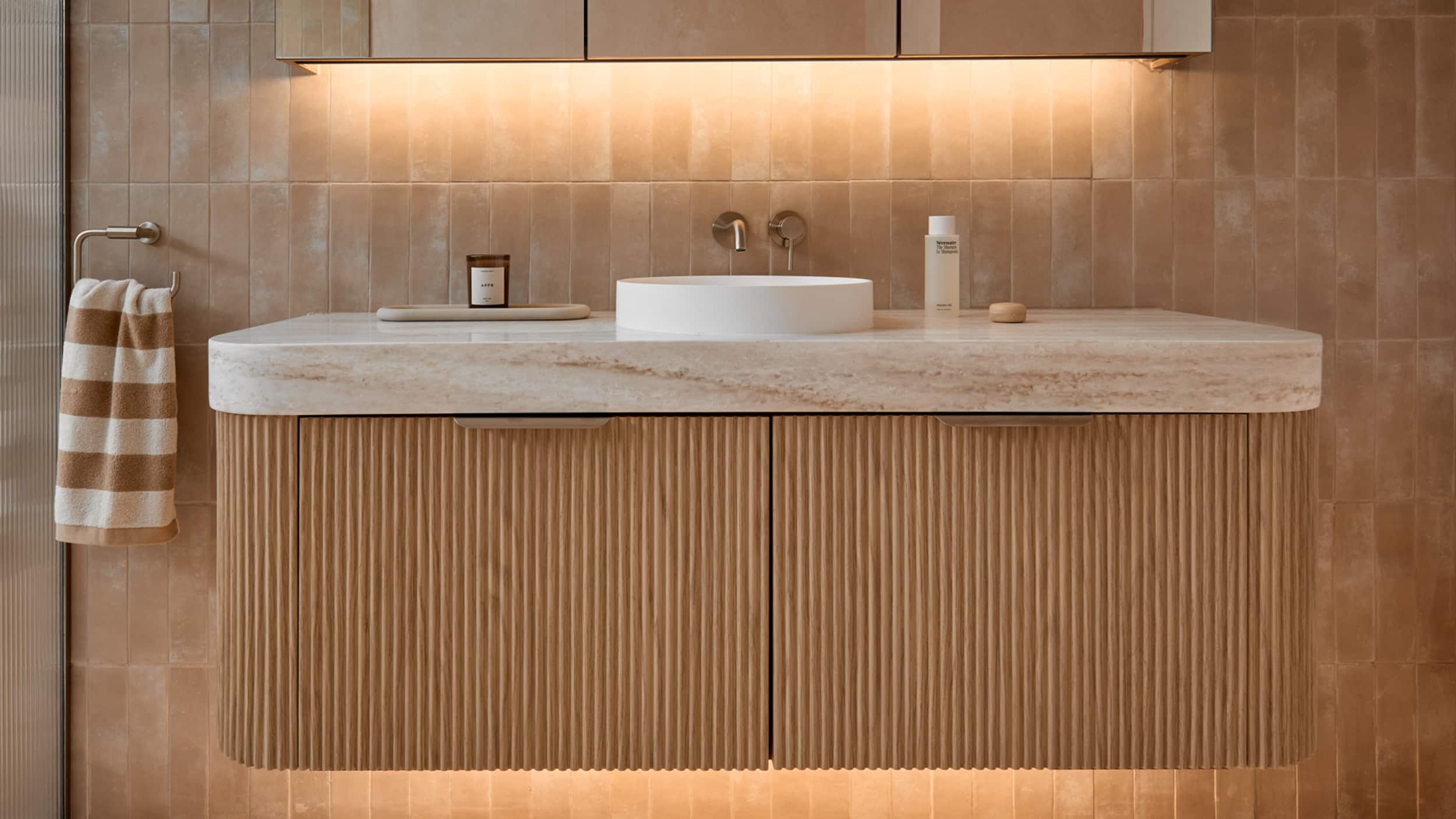 A luxurious bathroom featuring timber vanity, with curved edges, single basin, and LED lighting under the mirror and vanity