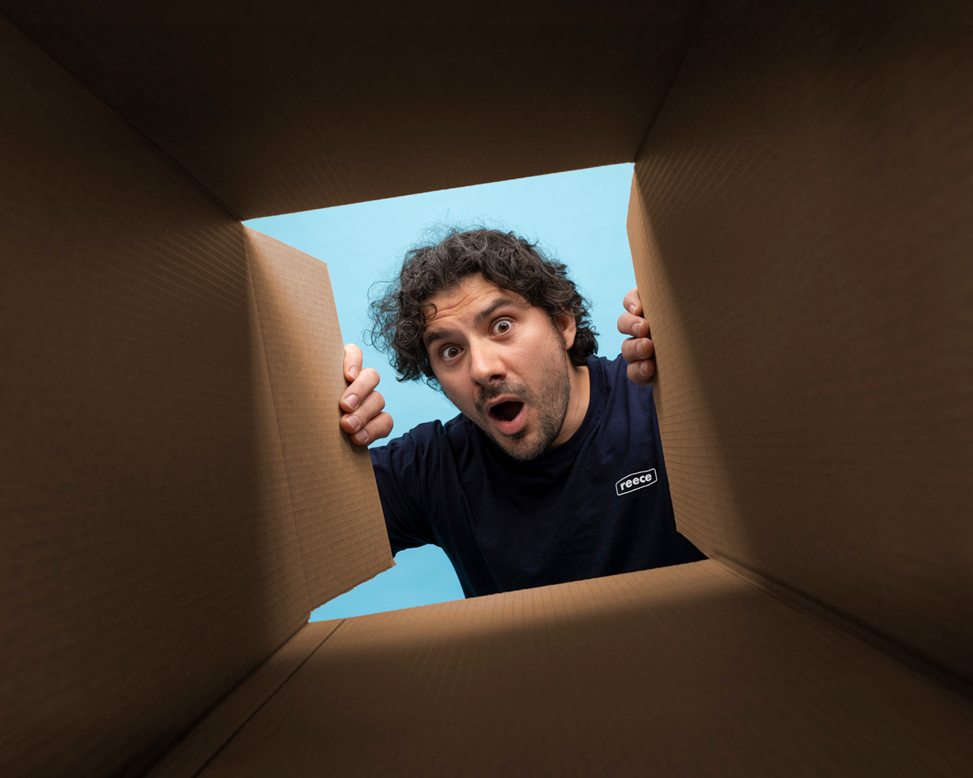A man in a navy blue Reece t-shirt looking into a cardboard box and directly into the camera.