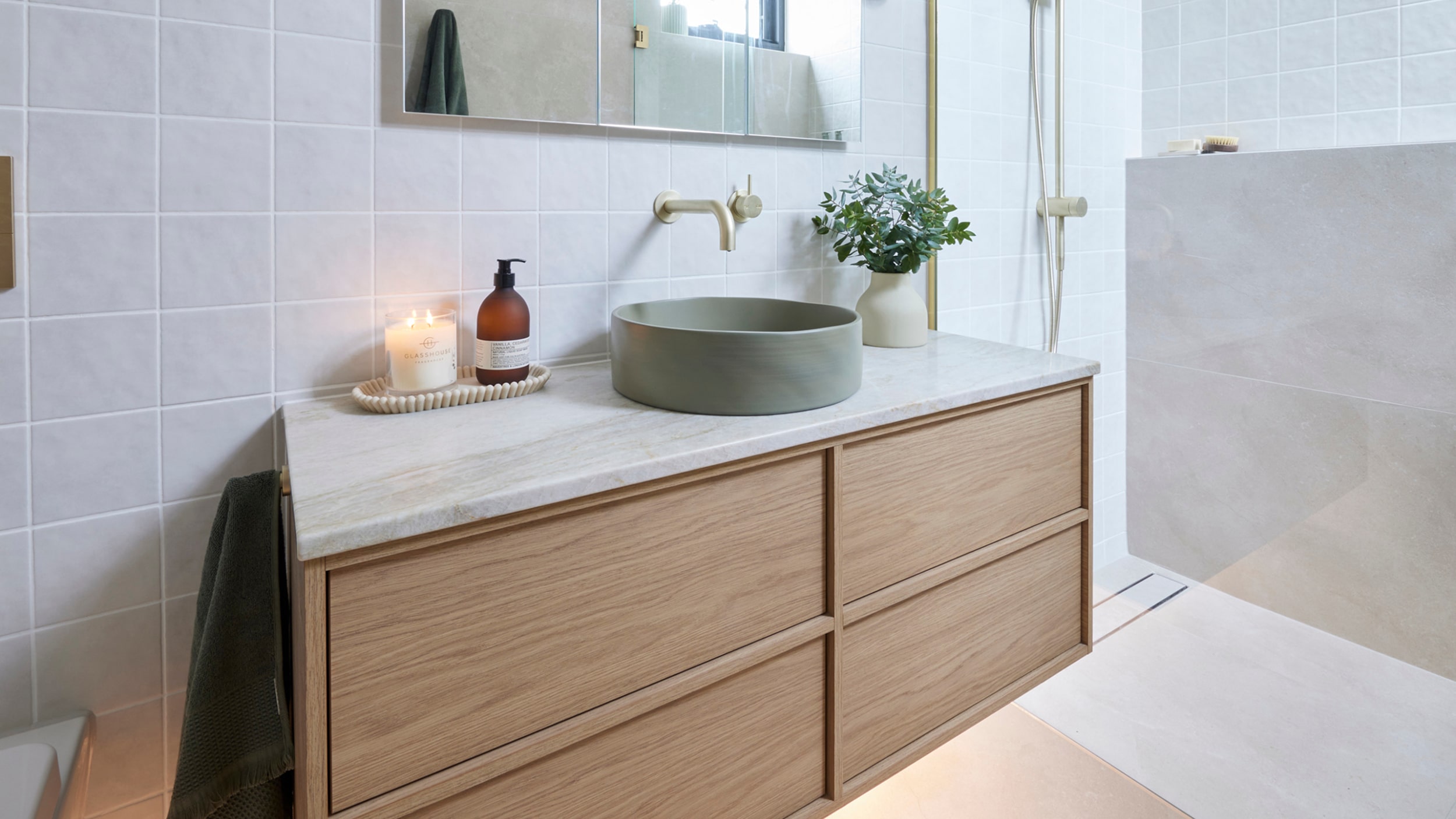 A luxurious light bathroom featuring a timber vanity, sage coloured basin and brushed tapware.