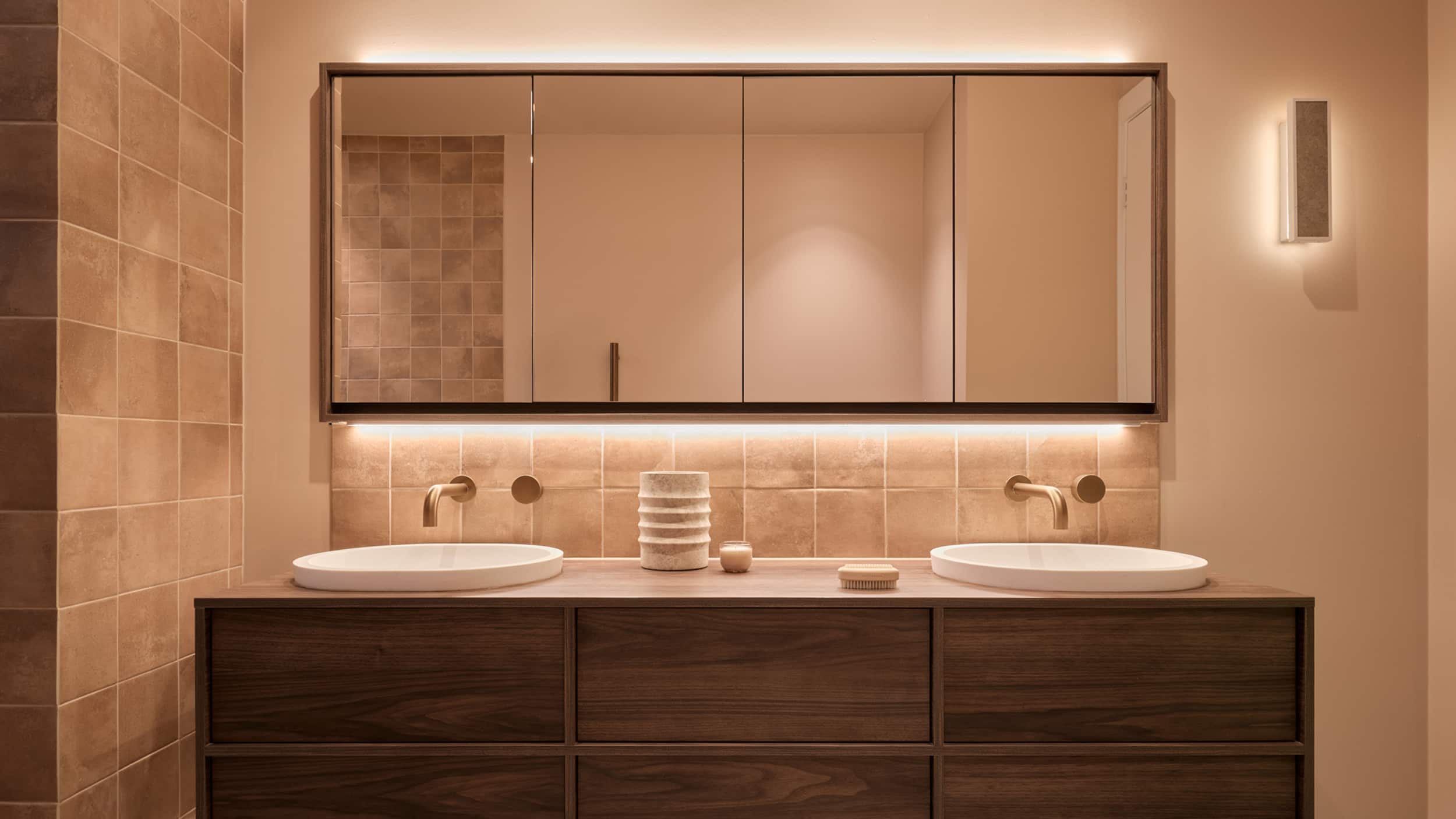 A spa-like bathroom with walnut-toned vanity, mirror cabinet with feature LED lighting, two basins and bronze tapware