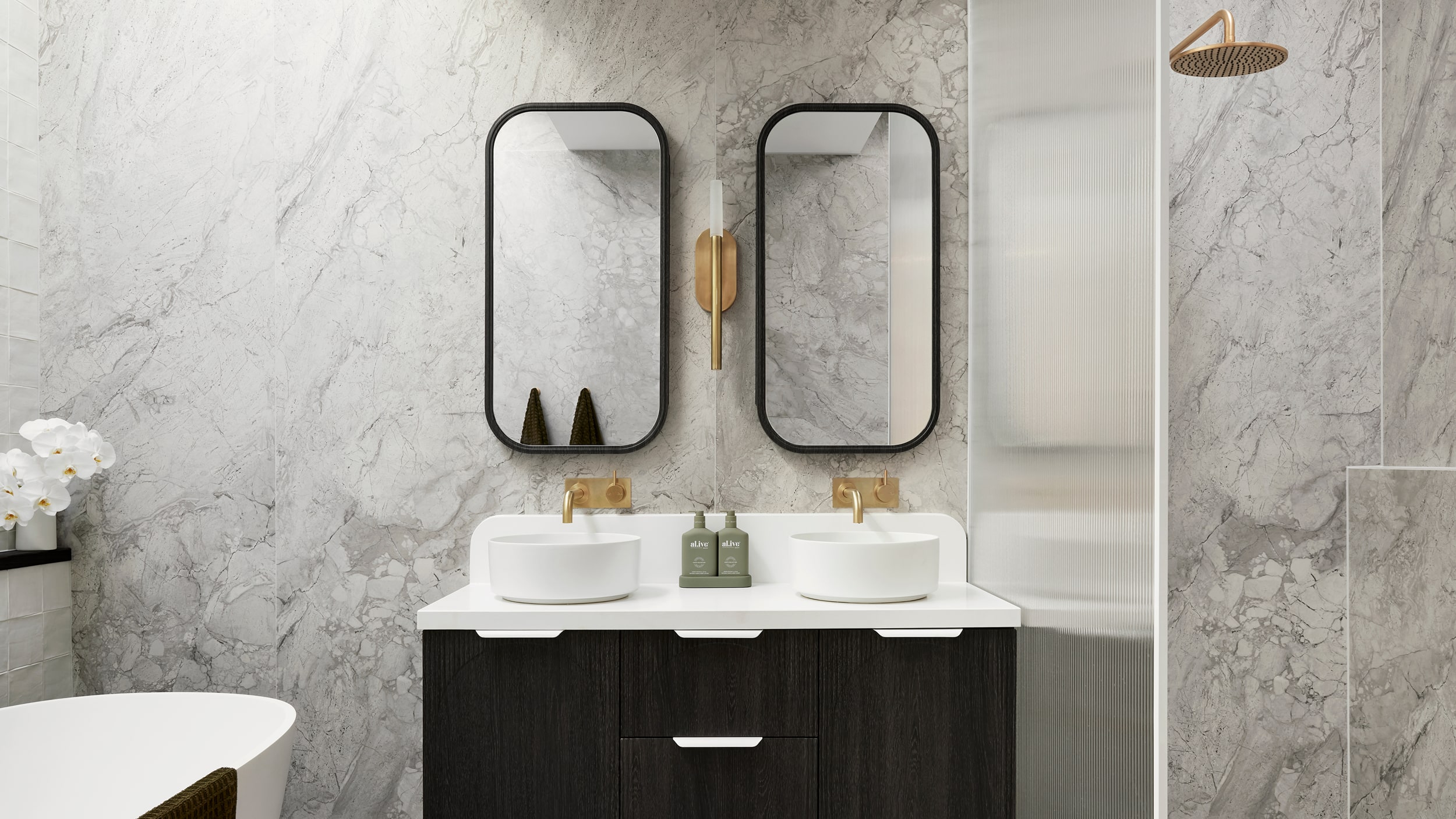A sleek, stylish bathroom featuring dark vanity, two white basins, brushed gold tapware and two mirrors, with a bathtub on the right, and a shower on the right.