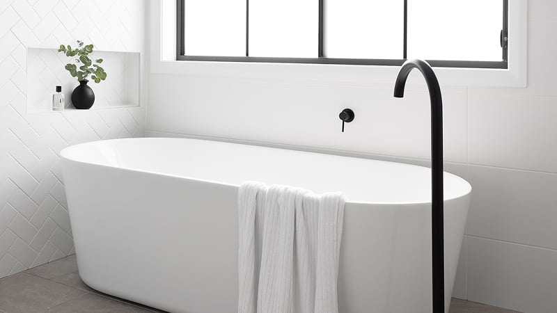 A classic, white freestanding bathtub paired with matte black tapware and floor-mounted bath outlet.