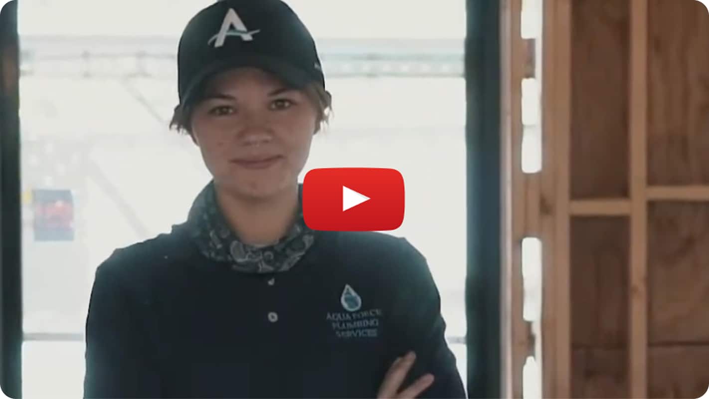 A still from a YouTube video, featuring a female plumber looking directly at camera.