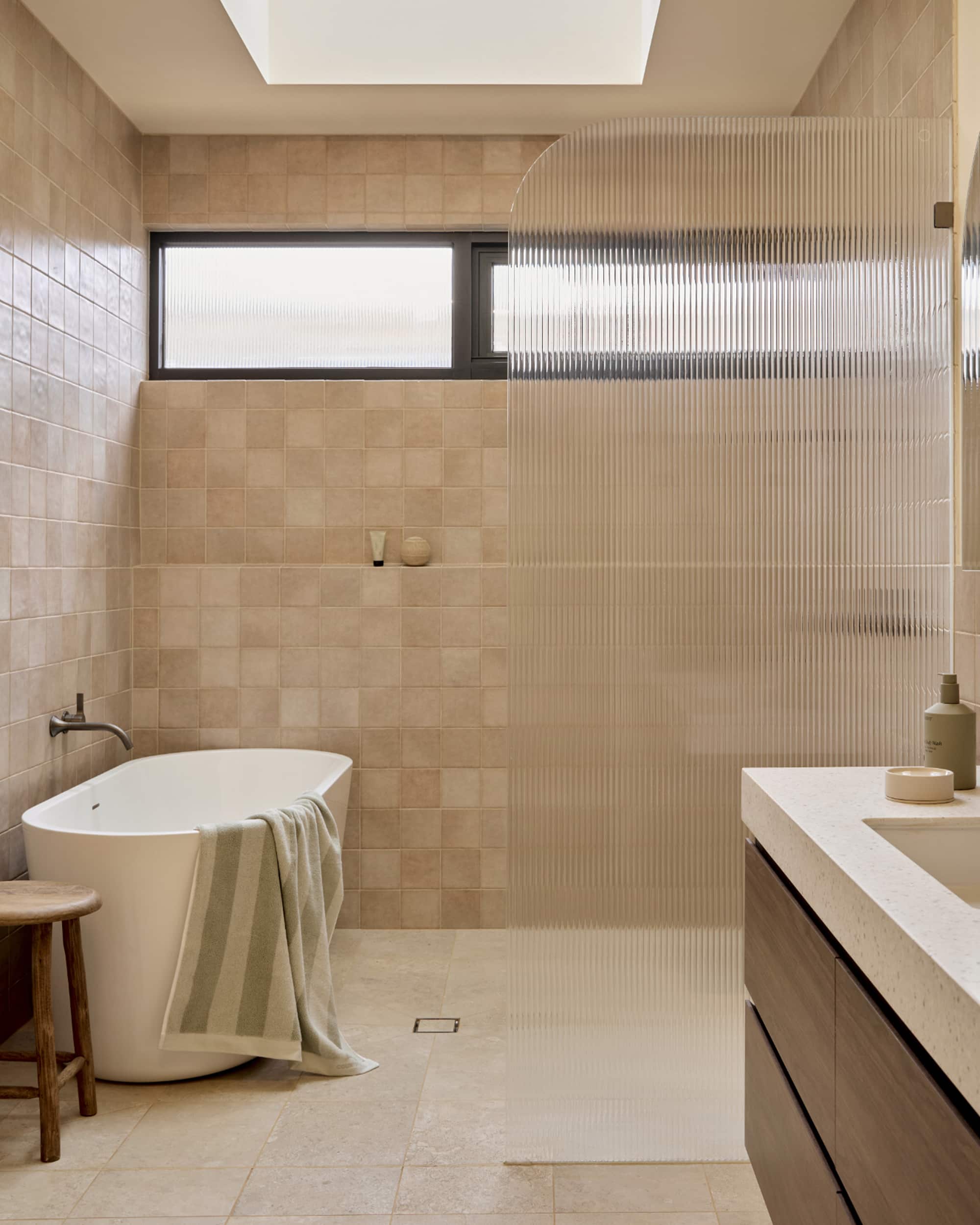 A spa-like bathroom featuring blush tile, freestanding bath next to an expansive shower with fluted glass screen, and timber vanity