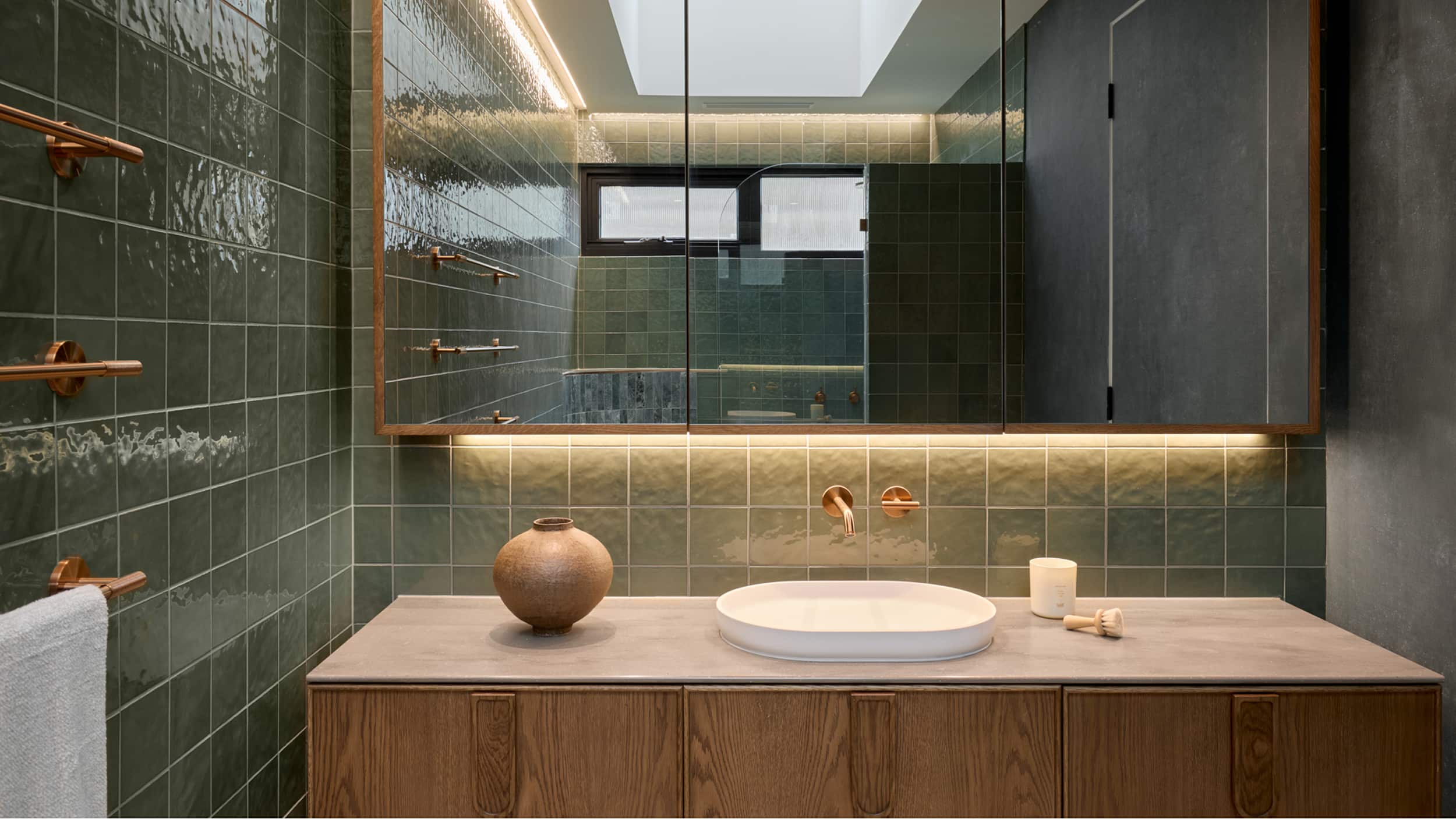 Sleek bathroom with timber vanity, white basin, green tile, and large mirror reflecting the shower