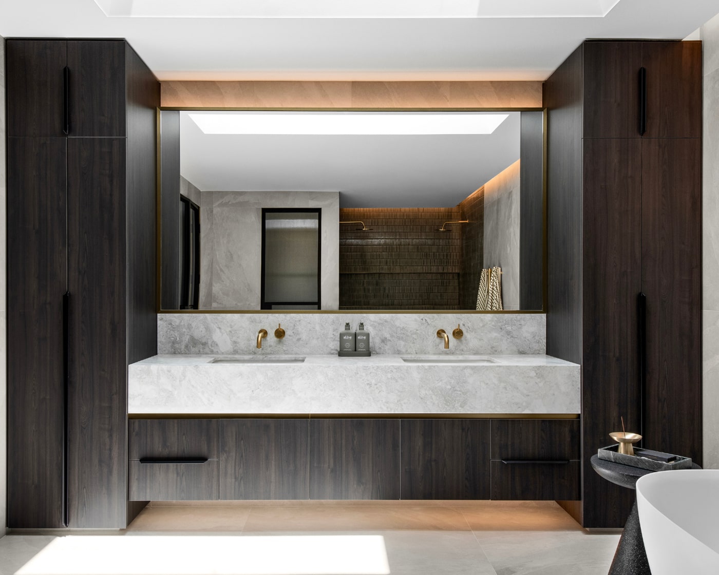 A stylish bathroom featuring a long marble vanity with large mirror, flanked by black cabinetry on either side.