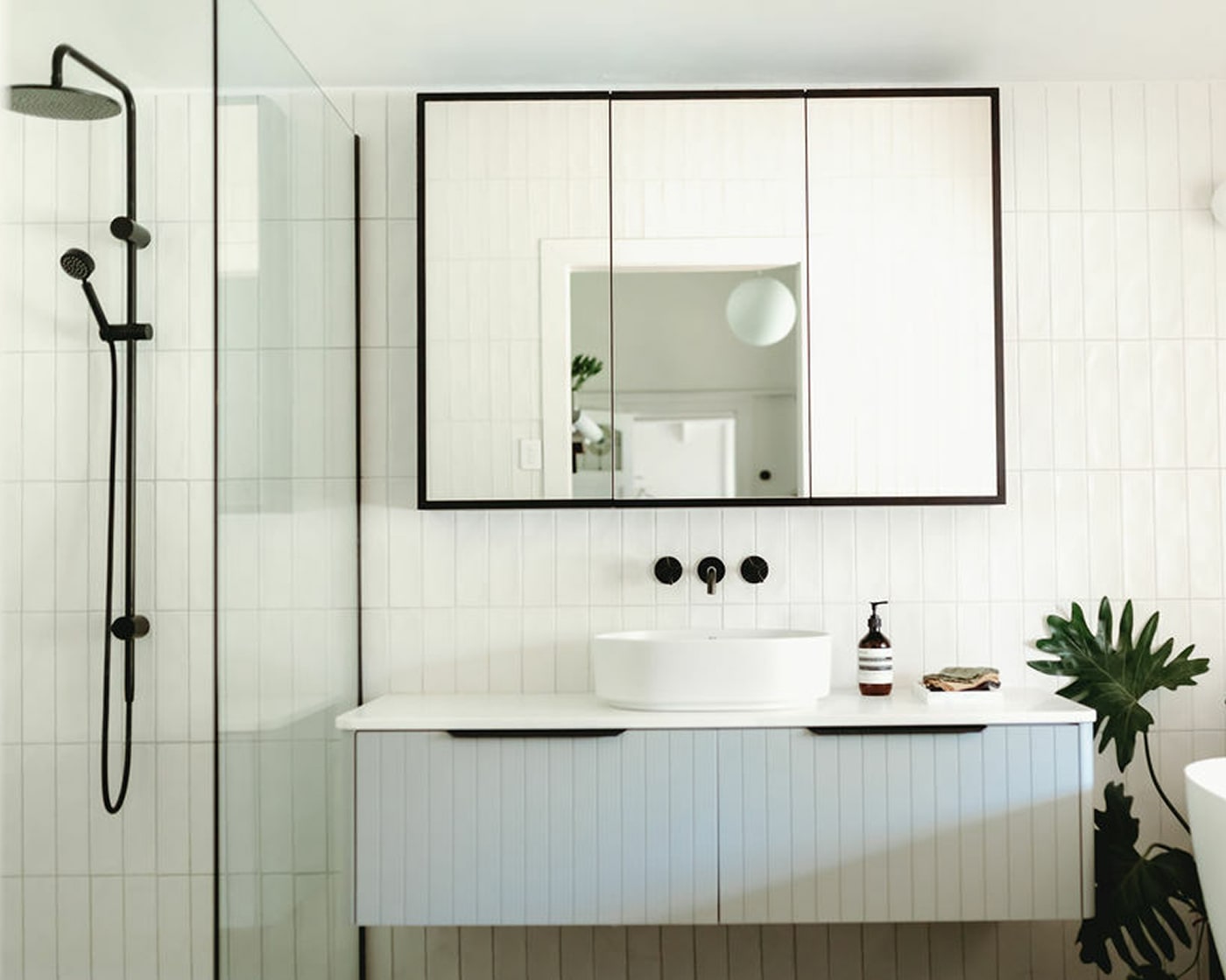 A stylish, light bathroom featuring walk in shower next to a shaker-style vanity, single white basin, with matte black tapware.