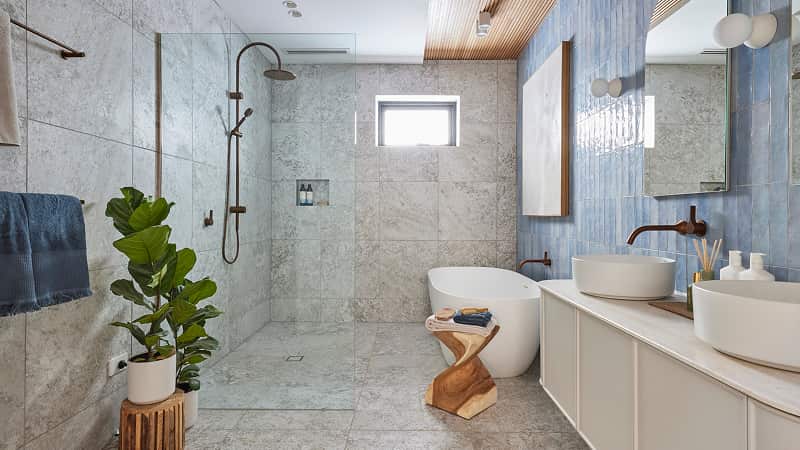 Large bathroom with walk in shower, deep bathtub, white vanity, brushed bronze tapware and blue-tiled feature wall