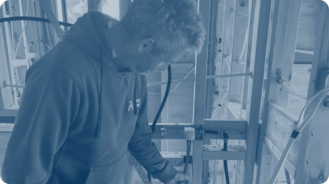 A plumber at work on a building site next to a timber wall frame.