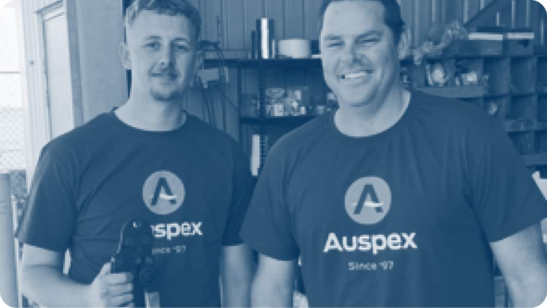 Two tradespeople, wearing Auspex t-shirts, smiling at camera.