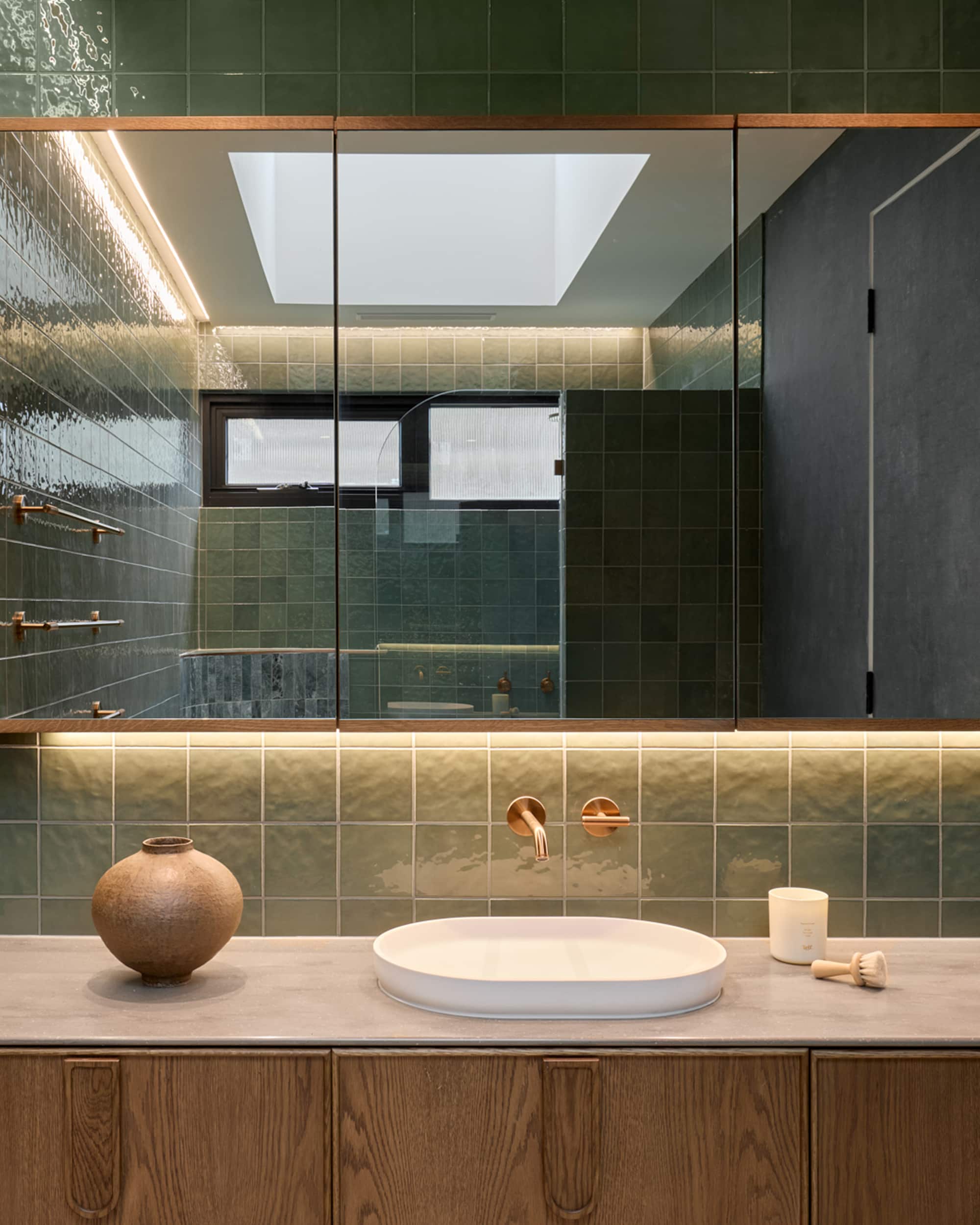Sleek bathroom with timber vanity, white basin, green tile, and large mirror reflecting the shower