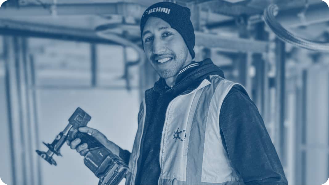 A plumber in a high-vis vest, smiling at camera and holding a hand tool.