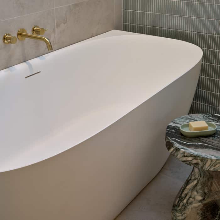 A deep, freestanding bath with brushed brass tapware, next to a light green feature tile wall
