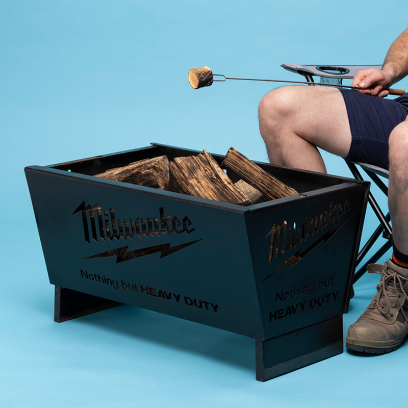 A man sitting next to a Milwaukee firepit, toasting a marshmallow.