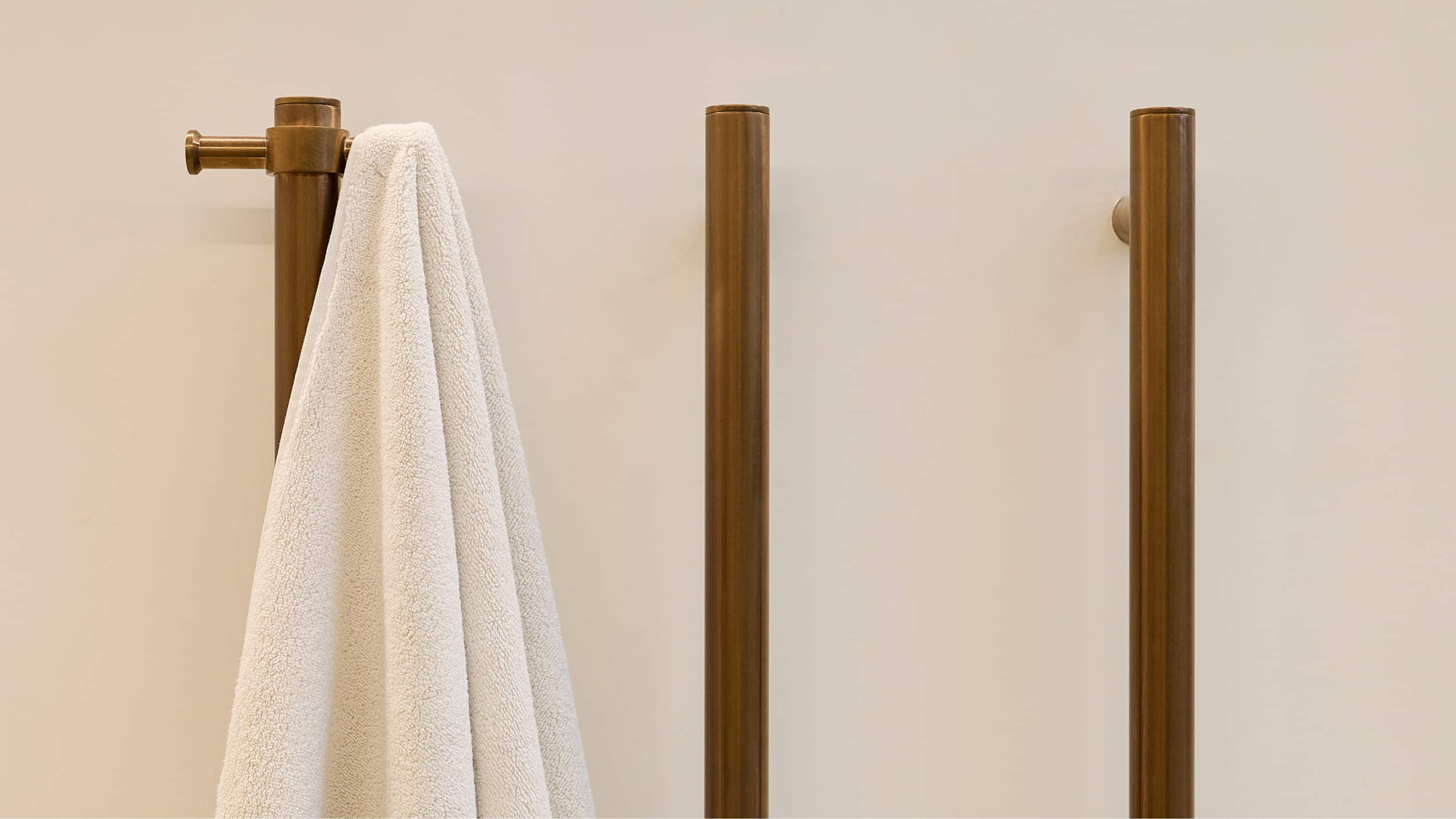 Three brushed bronze, vertical towel rails on a neutral wall, with a white towel hanging from the first rail