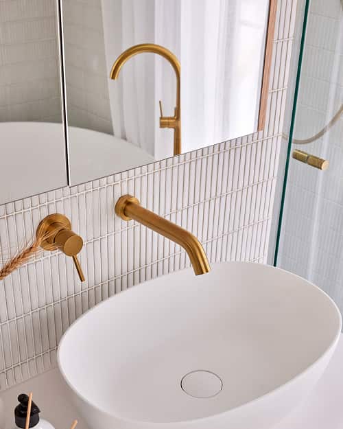 A white basin with brushed gold tap and mixer.