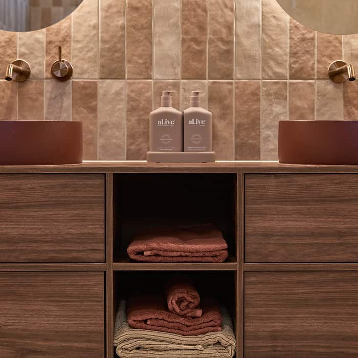 A timber vanity, two above counter basins, on a blush-coloured tile wall