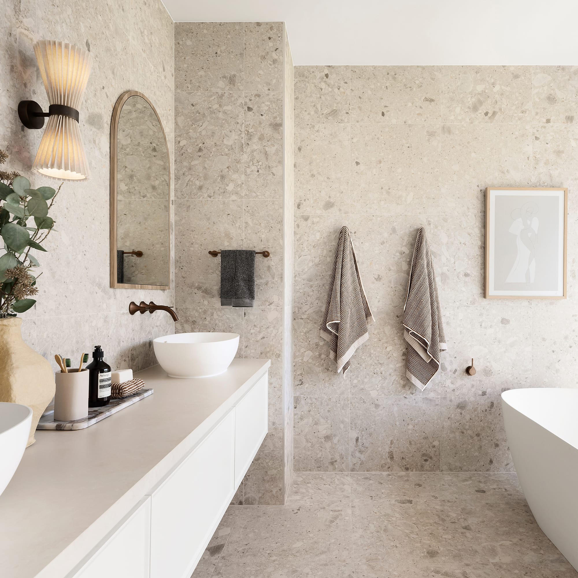 A spacious bathroom with a white bathtub and basins, paired with dark metal tapware showcasing a luxe, wellness spa aesthetic.