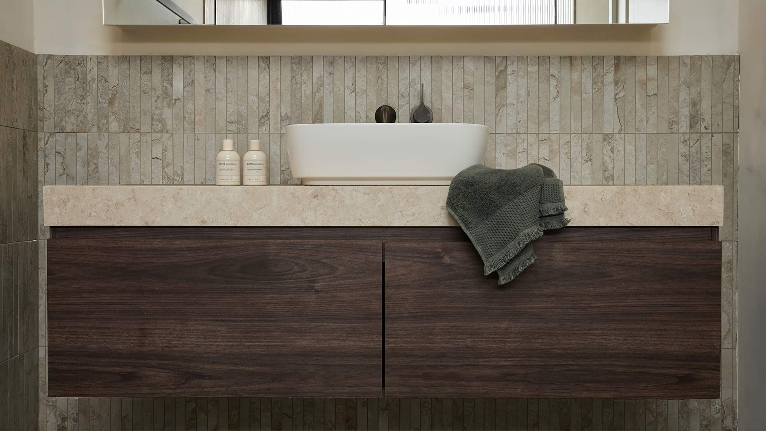 Dark timber vanity with single above counter basin, on a coffee-coloured tile wall