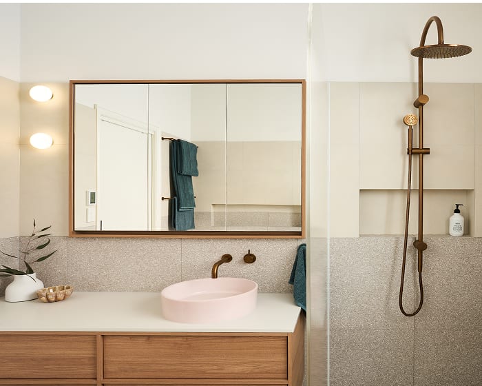 A sleek, stylish bathroom featuring a pink basin, wooden vanity, and dark brushed metal tapware, blending color and natural materials.