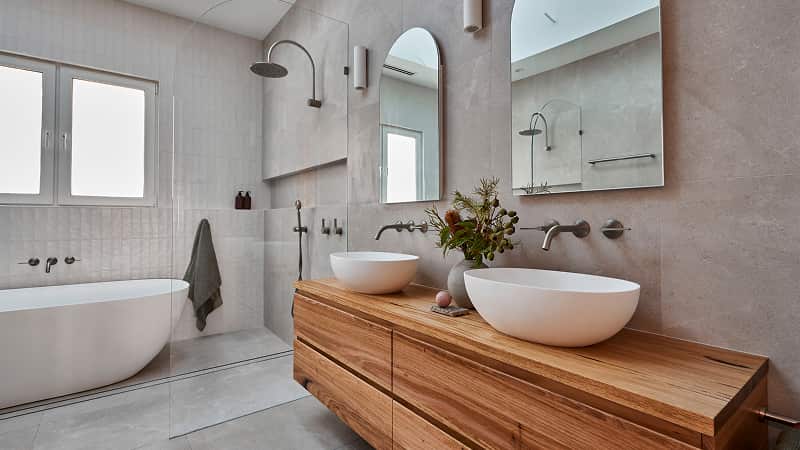 A light bathroom featuring double timber vanity, white above counter basins, arched mirrors and large shower room.