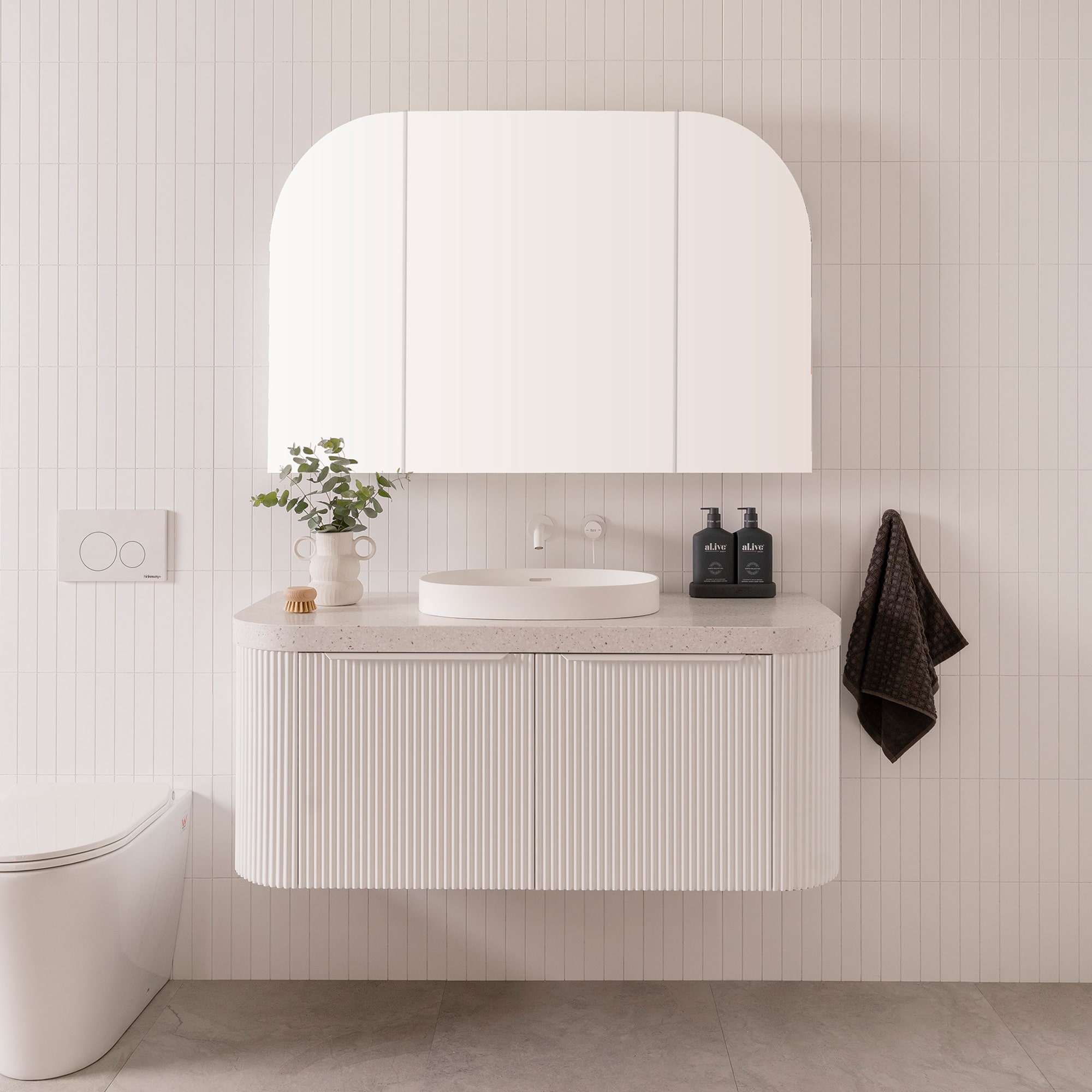 A modern bathroom featuring white walls, a white wooden vanity and a soft arched vanity mirror cupboard.