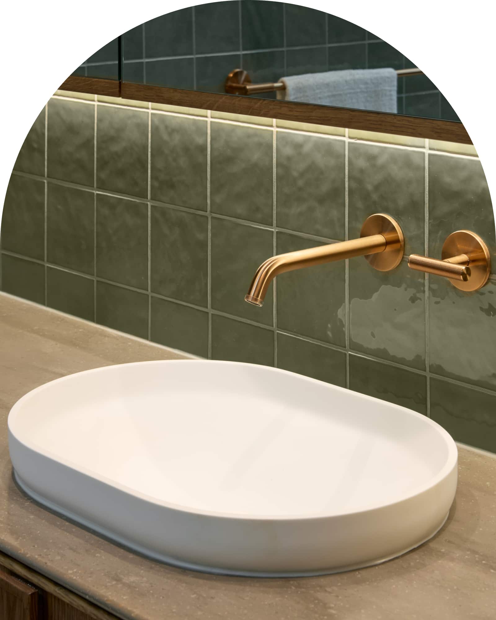 A white basin paired with brushed bronze tapware on a green-tiled wall