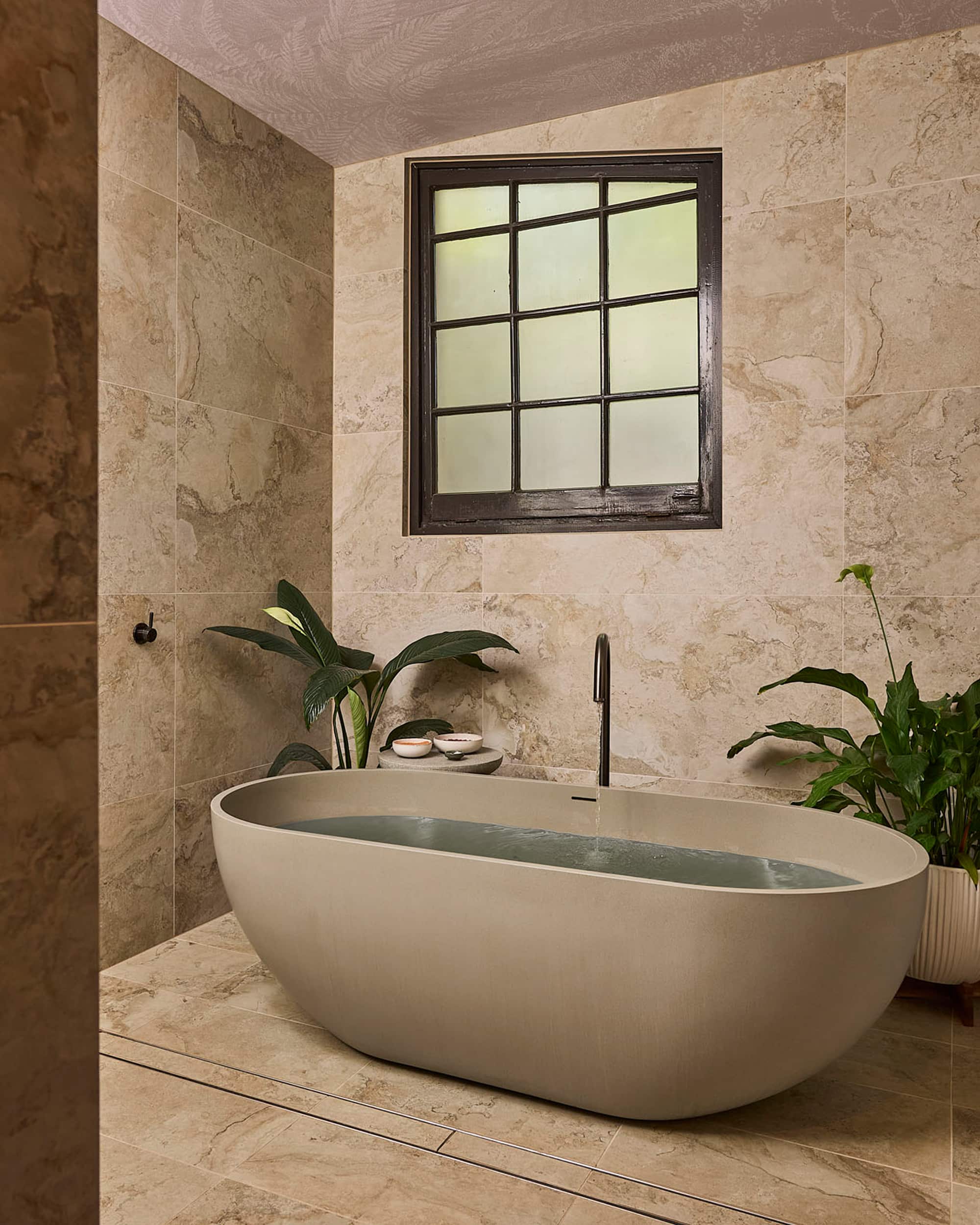 Spa-like bathroom, featuring a bathtub full of water, tiled walls and window