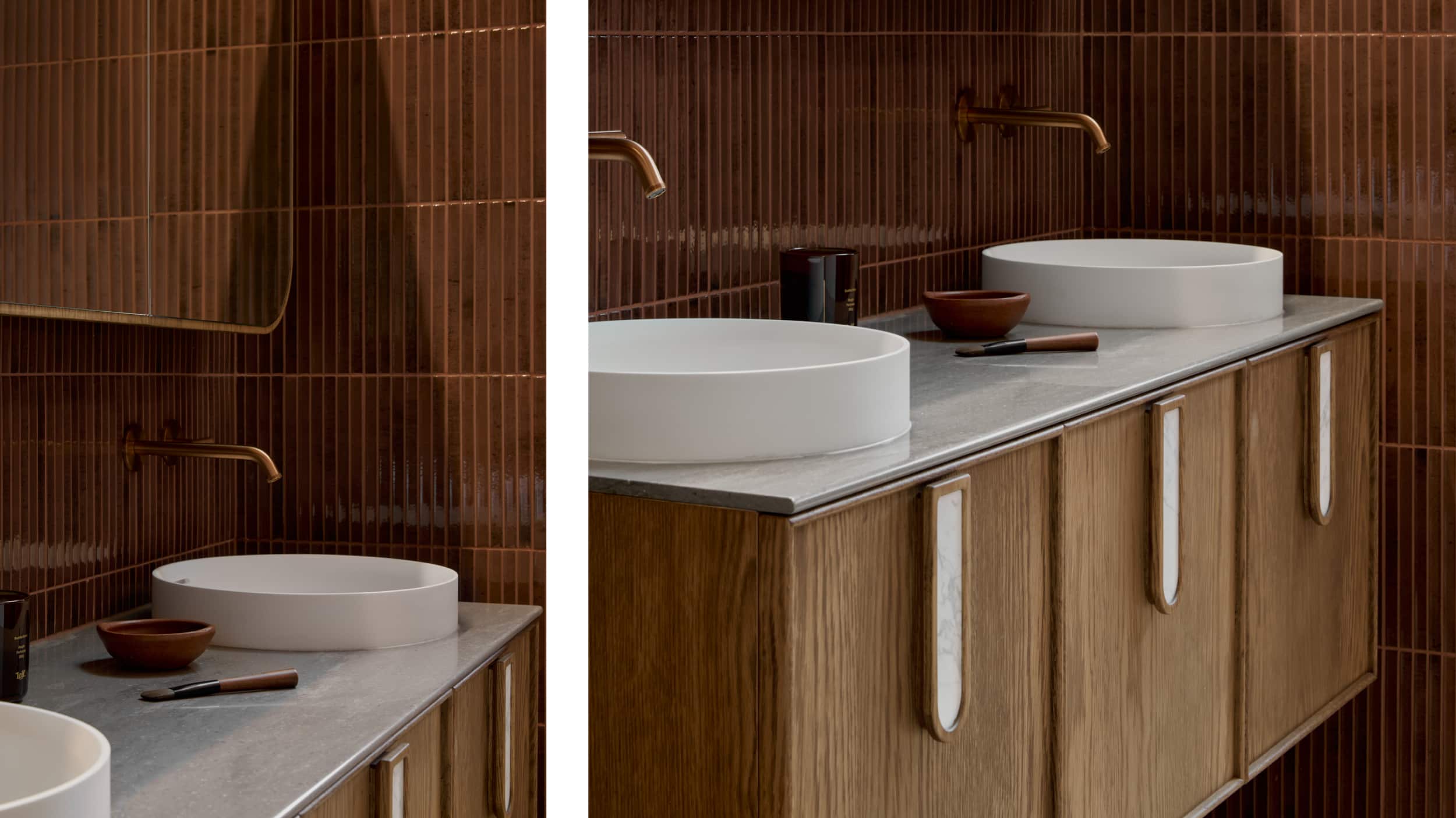 A moody, berry-hued bathroom featuring a timber vanity, above counter basins and brushed bronze tapware