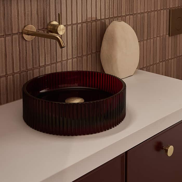 A deep red basin on a white countertop, paired with brushed gold tapware
