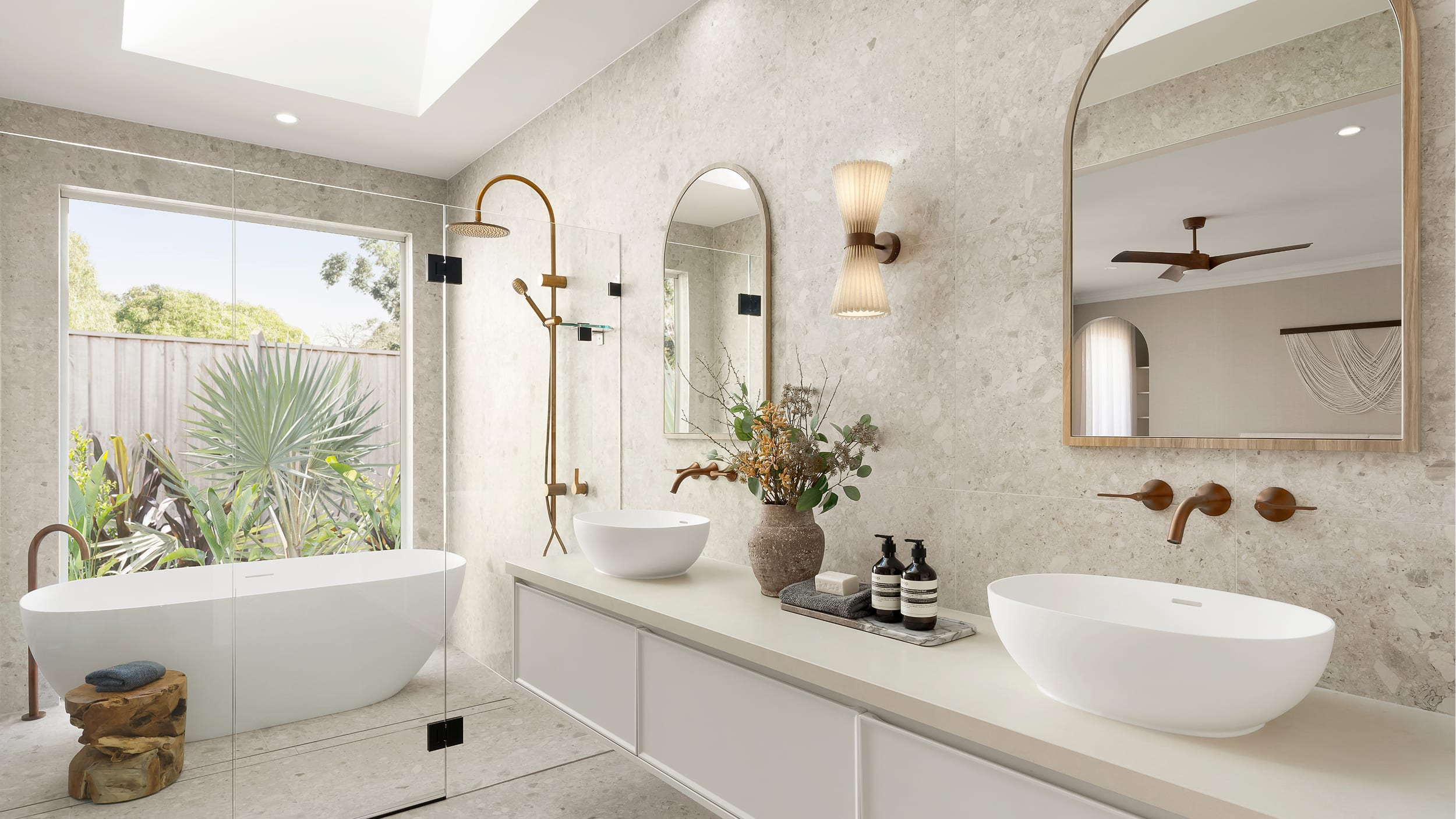 A well-designed, spacious, resort-style bathroom showcasing a large, freestanding bathtub, large double vanity, white basins and dark, brushed metal tapware and fittings.