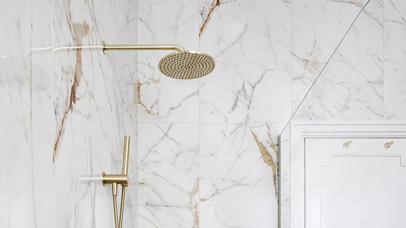 A luxurious white marble bathroom featuring a modern shower with a gold shower head.