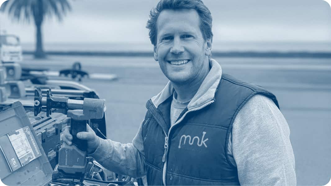 A plumber, holding a hand tool, smiling at camera.