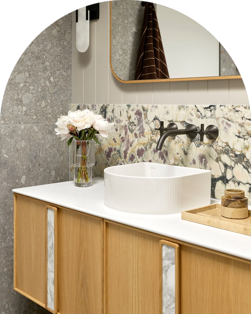 A luxurious bathroom featuring timber vanity, stone backsplash, white basin and statement matte black tapware.