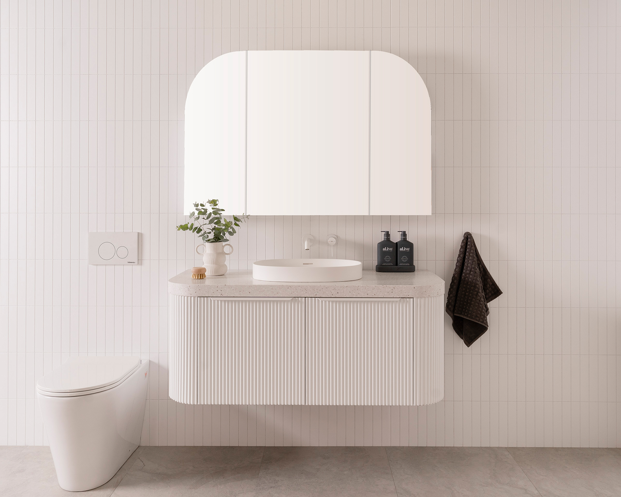 A modern bathroom featuring white walls, a white wooden vanity and a soft arched vanity mirror cupboard.