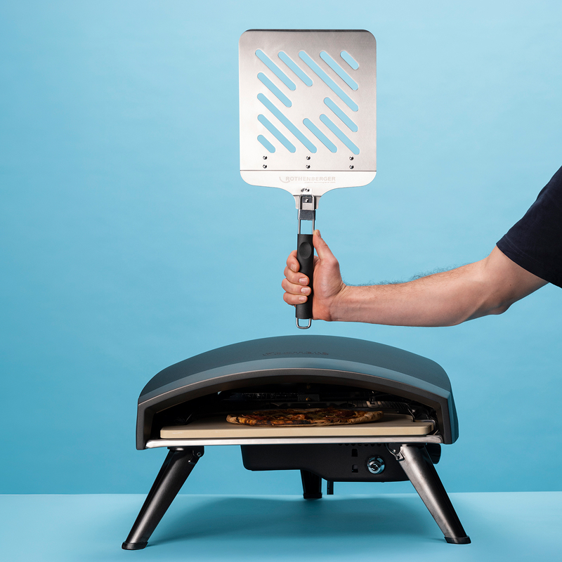 A Rothenberger pizza oven, and a man holding a pizza peel above it.