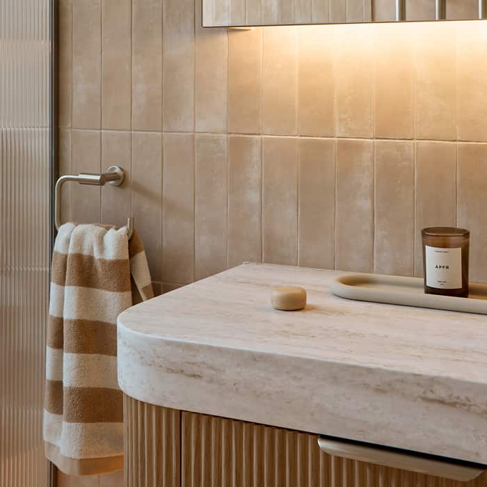 A spa-like bathroom featuring muted tile, timber vanity, mirrored cabinet with LED lighting, finished with a striped hand towel