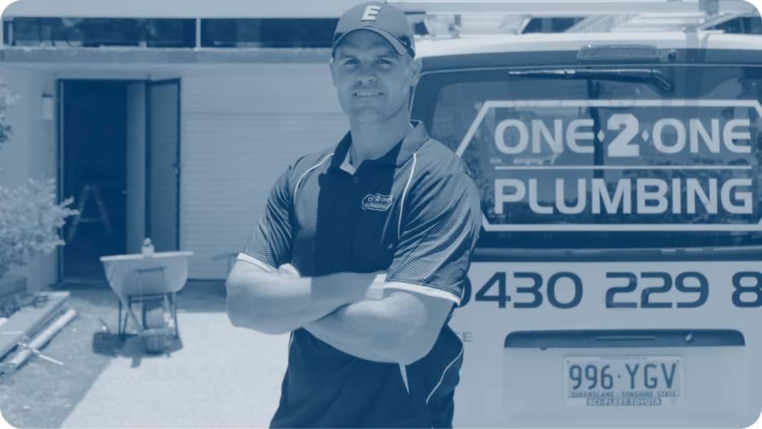 A plumber, standing next to a work van, smiling at camera while crossing his arms.