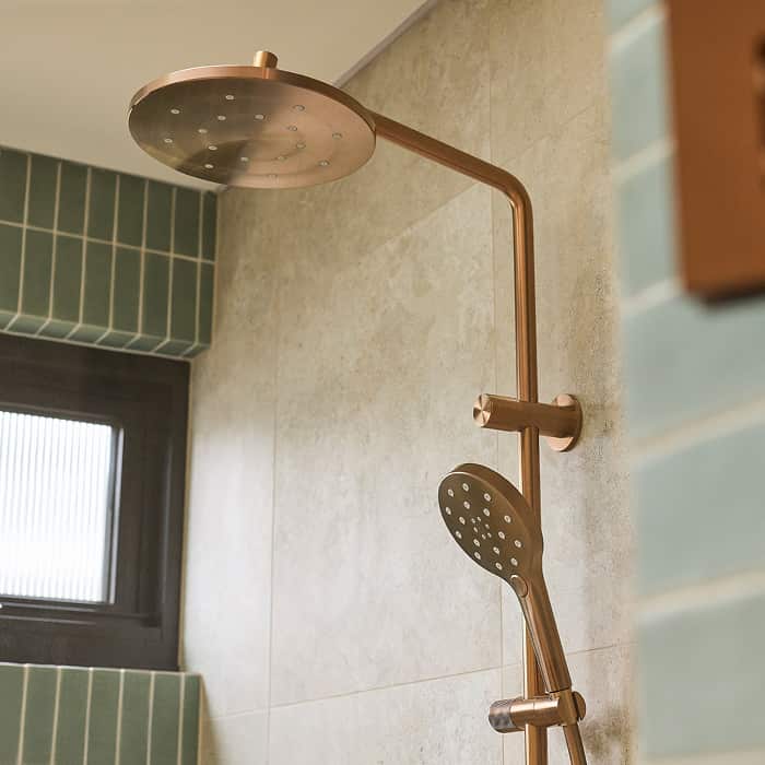 A brushed bronze shower head and hand shower in an expansive shower with light green feature tile wall