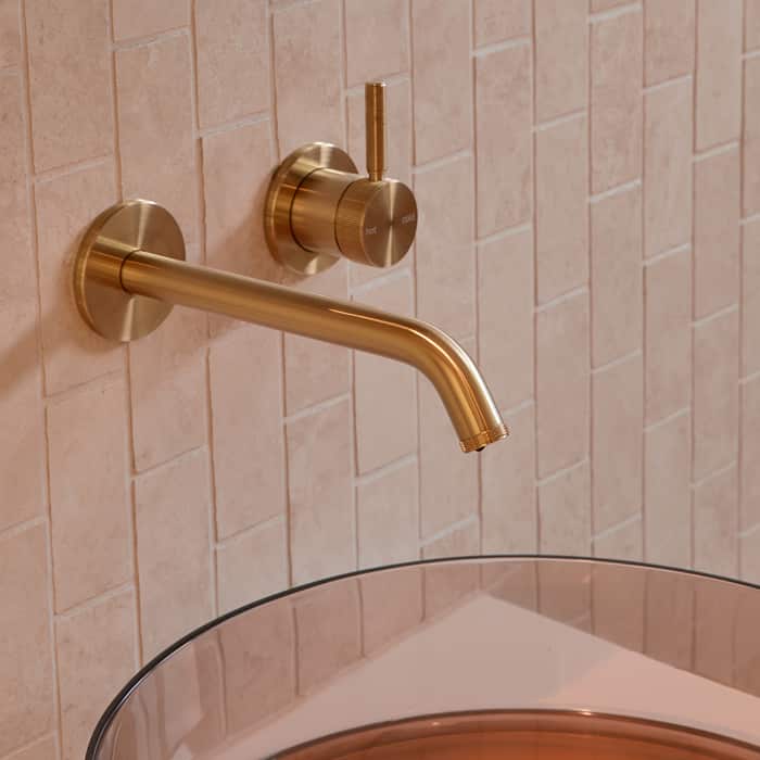 A brushed gold basin outlet and mixer on blush tile, with a resin basin